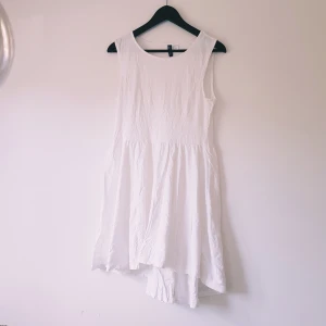 Vit ärmlös klänning från H&M Divided strl 40 - Superfin vit klänning från H&M Divided i storlek 40. Den är ärmlös med rund halsringning och har en lätt utsvängd kjol med asymmetrisk nederkant. Perfekt för varma dagar och enkel att styla med sneakers eller sandaler.  Helt skick dock obehandlade fläckar