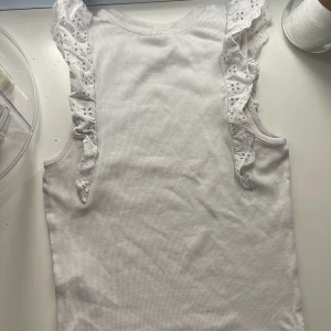 Vit ribbad topp med volanger  - Säljer denna fina vita ribbade topp med volanger! I stl 146-152.