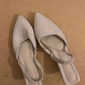 Vita pumps med spetsig tå och låg klack - Snygga vita pumps med spetsig tå och låg klack. Skorna har en öppen häl med smal rem runt ankeln och en stilren, ribbad textur på ovandelen. Perfekta för dig som gillar minimalistisk och trendig stil. De är dock lite vingliga att gå i men jag tror att det kan vara för att jag inte kan gå i klack. Så fina och eleganta.