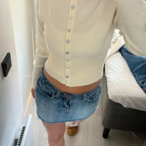 Blå vintage egengjord jeanskjol med fransig kant - Säljer en blå jeanskjol  med fransig rå kant och unika fickor bak. Kjolen har låg midja, bälteshällor och snygga detaljer med nitar på bakfickan. Materialet är 98% bomull och 2% elastan för en skön passform.