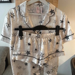 Stjärnmönstrade pyjamasset Victoria's Secret - Snyggt pyjamas set från Victoria's Secret i glansigt, silkesliknande material. De är vita med svarta och guldiga stjärnor, har elastisk midja och svarta kantdetaljer. Storlek Xs-Xxs
