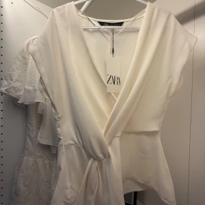 Vit omlottopp från Zara - Säljer en snygg vit omlottopp från Zara med knyt i midjan. Helt ny med prislapp. Orginalpris 329 och säljer för 299