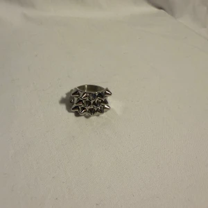 Silvrig ring med nitar, storlek 8 - Cool och chunky ring i silverfärgad metall med flera spetsiga nitar runt hela bandet. Perfekt statement piece för dig som gillar edgy och alternativ stil. Ringen är bred och har en riktigt tuff vibe.