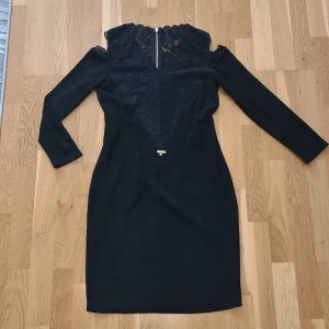 Svart spetsklänning från Jusdepom - Supersnygg svart klänning från Jusdepom med lång ärm och spetsdetaljer upptill. Öppen vid axlarna. Klänningen har en dragkedja i ryggen. Mjukt, velourliknande material. 