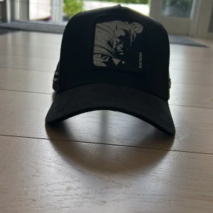 Svart Batman keps från Capslab - Snygg svart keps från Capslab med Batman-tryck framtill och mesh på sidorna för extra ventilation. Kepsen har böjd skärm, broderad Batman-logga på sidan och justerbar passform. Perfekt för dig som gillar superhjältar och vill sticka ut.