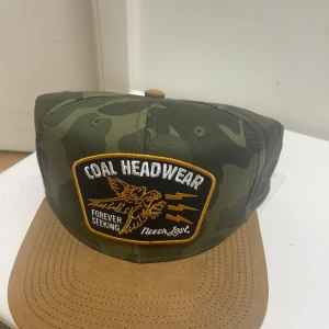 Camouflage keps från Coal Headwear - Snygg keps från Coal Headwear med klassiskt camouflage-mönster i gröna toner och brun skärm. Framtill finns en broderad patch med örn och text. Justerbar snapback baktill för perfekt passform. Perfekt accessoar för en cool streetstyle.