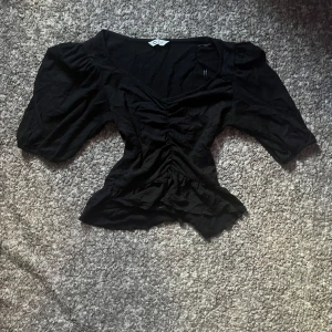 Svart blus med puffärmar XS - Svart blus från Cubus i storlek XS. Bara använd en gång och sedan bara blivit tvättad. Med snygga puffärmar och v-ringning. Toppen har rynkade detaljer framtill och en figurnära passform som framhäver midjan. Perfekt för dig som gillar trendiga och feminina plagg. 