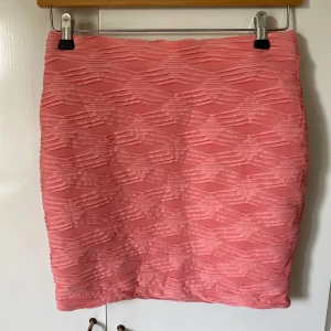 Rosa kortkjol med strukturmönster - Säljer en snygg rosa kortkjol med coolt strukturmönster i tyget. Kjolen har en tight passform och är perfekt för dig som gillar att sticka ut lite extra. Materialet känns mjukt och stretchigt, vilket gör den bekväm att bära hela dagen.