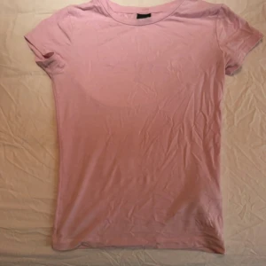 Ljusrosa basic t-shirt i bomull - Enkel och stilren ljusrosa t-shirt i mjuk bomull. Modellen är klassisk med rund halsringning och korta ärmar. Perfekt att matcha med jeans eller kjol för en clean look. T-shirten är enfärgad utan tryck eller detaljer. (Lite genomskinlig)