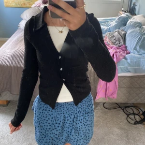 Svart ribbad kofta från H&M Divided - Svart ribbad kofta från H&M Divided i storlek XXS. Koftan har klassisk krage, långa ärmar och knäpps med tre knappar framtill. Tillverkad i mjuk och stretchig polyesterblandning som sitter snyggt och är lätt att styla till olika outfits. Kommer att noppa av den innan jag skickar den!🥰🥰