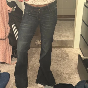 Mörkblå bootcut jeans med rosa detalj - Säljer ett par mörkblå bootcut jeans från weekday med snygga slitningar och kontrastsömmar. Jeansen har låg midja och en rosa broderad logga bak i linningen. Klassisk femficksmodell i stretchigt denimtyg som sitter riktigt snyggt.