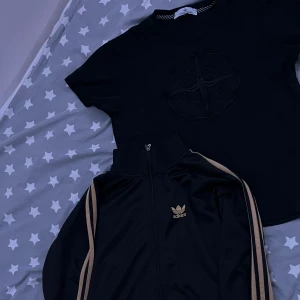 Svart Adidas track med guldiga detaljer med stone island t-shirt - Säljer en svart Adidas track jacket med guldiga detaljer längs ärmarna och Adidas logga på bröstet. Och en stilig stone island t-shirt. Säljer addidas tröjan för 500kr och t-shirten för 250kr enskilt om man så önskar. Annars säljer båda plaggen för 600kr