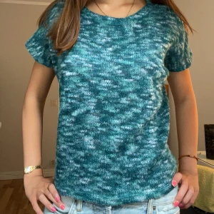 Blåmelerad stickad kortärmad tröja - Säljer en blåmelerad stickad tröja med korta ärmar och rund hals. Tröjan har en avslappnad passform och är perfekt för dig som gillar en chill och bekväm stil. Melerat mönster i olika blå toner ger en unik look.🍒står ingen storlek men skulle säga S