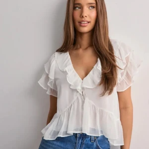 Vit volangblus med v-ringning - Supersöt vit blus med v-ringning o volangdetaljer i storlek XS . Köpt för 299 kr på nelly. Bara prövad💓 