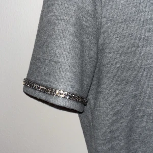 Grå ribbad topp med glittriga detaljer - Snygg grå ribbad topp med korta ärmar. Ärmsluten är dekorerade med glittriga paljetter som ger en extra touch. Perfekt för dig som vill ha något enkelt men ändå sticker ut lite.