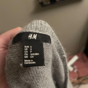 Grå stickad tröja från H&M - Mysig grå stickad tröja från H&M i storlek S. Tröjan har en enkel och klassisk design med rund halsringning och långa ärmar. Perfekt för lager-på-lager och chill dagar. Ribbstickade muddar vid ärmslut och nederkant ger en snygg finish.