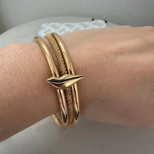 Guldigt armband Diane von Furstenberg - Stilrent armband i guldton från Diane von Furstenberg. Armbandet har tre band, varav ett är flätat och två är släta, med DVF klassiska läpp ikon detalj framtill