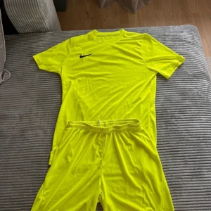Neongul Nike fotbollströja Dri-FIT M - Säljer en neongul fotbollströja från Nike i Dri-FIT-material, perfekt för träning eller match. Tröjan är kortärmad och tillverkad i 100% polyester för maximal andningsförmåga. Klassisk rund hals och svart Nike-logga på bröstet.