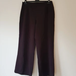 Bruna vida byxor från NP Collection strl 42 - Mörkbruna byxor från NP Collection i storlek 42. Byxorna har en rak och vid passform med hög midja och är tillverkade i ett mjukt tyg som känns bekvämt. Perfekta för dig som gillar en stilren och enkel look.  Dragkedja på sidan Helt & fint skick