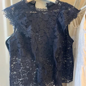 Mörkblå spetsblus från Zara - Supersnygg mörkblå blus från Zara i spets med blommigt mönster. Ärmlös modell med vacker volangkant vid axlarna och hög halsringning. Perfekt för dig som vill ha en feminin och trendig look!💙