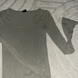 Grön långärmad topp med rund hals - En enkel och stilren grå långärmad topp med rundad halsringning. Perfekt att styla med jeans eller kjol för en clean look. Tunn och mjuk i materialet, sitter skönt mot kroppen och passar året runt.