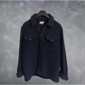 Mörkblå overshirt från Murrey i ullblandning - Snygg mörkblå overshirt från Murrey i ullblandning. Skjortan har klassisk krage, två stora bröstfickor med lock och knappar framtill. Perfekt lager på lagerplagg med avslappnad passform och långa ärmar.
