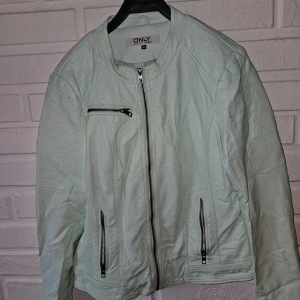 Mintgrön skinnjacka från ONLY - Snygg mintgrön skinnjacka från ONLY med coola detaljer som dragkedjor framtill och på fickorna. Jackan har rundad krage, quiltade axlar och lång ärm. Perfekt för dig som vill sticka ut med en fräsch färg och edgy look.   Den har fått mörka märken på ryggen när den hängt i garderoben, har inte försökt få bort det.  Har även fått märken på insidan armarna.   Annars i bra skick och väldigt snygg att bära – perfekt för dig som gillar second hand och vill ge jackan ett nytt liv!
