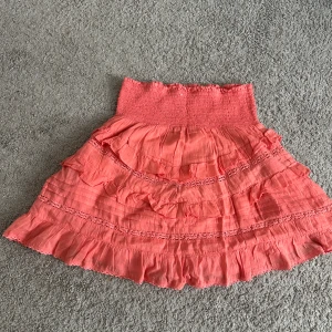 Korallrosa kjol med volanger  - Söt korallfärgad volangkjol från Kappahl! Använd ett fåtal gånger och har inga defekter alls. Säljer pågrund av att den inte används!💞