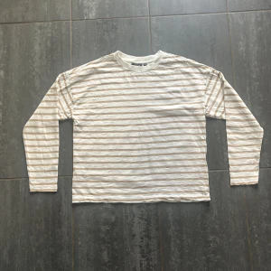 Randig långärmad tröja KappAhl  - Säljer en vit och beige långärmad tröja från KappAhl i storlek XS. Tröjan har tunna horisontella ränder och en klassisk rund halsringning med ribbad kant. Perfekt för dig som gillar en enkel och stilren look.