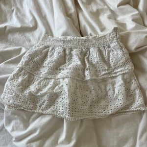 Vit broderad kortkjol med volang - Superfin vit kortkjol i bomull med broderade blommor och volangdetaljer. Kjolen har bred resår i midjan och är fodrad för extra komfort. Perfekt för sommarens alla tillfällen och ger en söt och fräsch look.