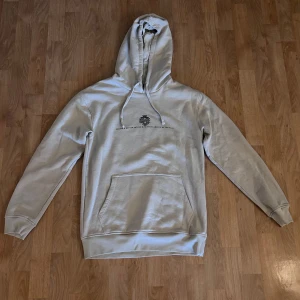 Beige hoodie med döskalletryck LCW Casual - Snygg beige hoodie från LCW Casual i storlek S. Framsidan har en liten svart print och baksidan pryds av ett stort, detaljerat döskalletryck i svart. Tröjan har huva med snörning och en klassisk magficka. 