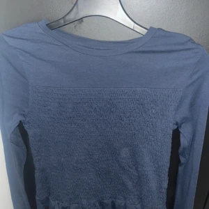 Blå långärmad topp med smock - Supersnygg blå långärmad topp från Gina Tricot i storlek 158/164. Toppen har smockat parti framtill som ger en cool struktur och sitter skönt. Perfekt till jeans eller kjol för en chill och trendig look.