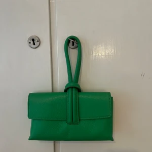 Grön axelväska i skinn med knyt - Snygg grön axelväska i skinn med stilren design och cool knyt-detalj på handtaget. Perfekt storlek för det viktigaste och ger en poppig färg till din outfit. Köpt i Rom. Finns liknande på Åhléns nu för cirka 1000kr 