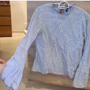 Blus från Vero Moda - Ljusblå randig blus från Vero Moda i stlk S. Utsvängande armar och volanger vid kragen, plus öppning med knapp mot ryggen. Väldigt bra skick. Återpublicerad annons! 