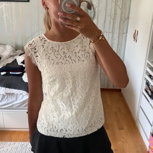 Vit spetsblus med kort ärm - Superfin vit blus i spets med snyggt mönster och små fransiga detaljer vid ärmslut. Blusen är ärmlös med rund halsringning. Perfekt att styla med kjol eller jeans för en fräsch look.🥰