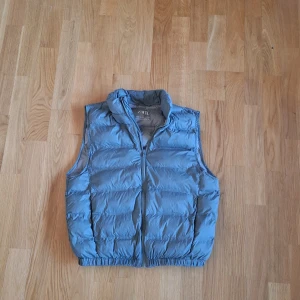 Blå dunväst från Zara, storlek 152-160 - Snygg grön dunväst från Zara med hög krage och breda, quiltade kanaler. Västen har dragkedja framtill och elastisk nederkant för en skön passform. Perfekt att slänga över en hoodie när det är kyligt ute. Pris kan diskuteras! Fråga på om ni har frågor