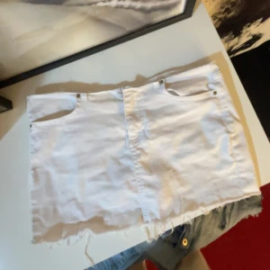 Vit jeanskjol med fransig kant - Vit kort jeanskjol med rå, fransig nederkant och klassiska fickor fram och bak. Kjolen har en rak passform och synliga sömmar, perfekt för en chill och trendig look. Passar till sneakers eller boots för en cool vibe.