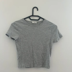 Grå croppad topp från Gina Basics - Enkel och stilren grå croppad topp från Gina Tricot Basics. T-shirten har rund halsringning och korta ärmar. 