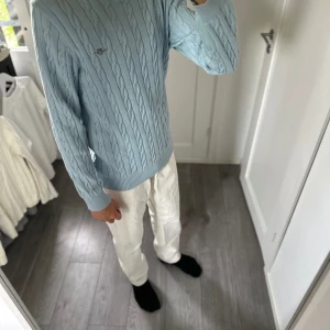 Ljusblå kabelstickad tröja från GANT - Säljer en ljusblå kabelstickad tröja från GANT i storlek M. Tröjan har rund halsringning, ribbade muddar och ett broderat GANT-emblem på bröstet. Perfekt för dig som gillar klassisk och stilren preppy-look.