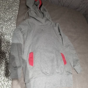 Grå hoodie med rosa detaljer - Säljer en grå hoodie med rosa detaljer vid fickorna och insidan av huvan. Tröjan har långa ärmar, stor huva med dragsko och en klassisk känguruficka framtill. Perfekt för chill dagar eller när du vill vara extra bekväm.
