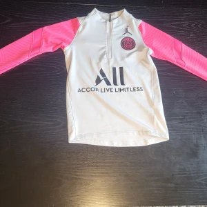 PSG x Jordan långärmad fotbollströja XS - Snygg PSG x Jordan långärmad fotbollströja i vitt med rosa ärmar och svart tryck framtill. Tröjan har halv dragkedja, Paris Saint-Germain-logga på bröstet och är tillverkad i ett lätt och sportigt material som andas. Perfekt för träning eller match.