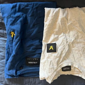 2 Lyle & Scott t-shirts blå & beige - Två snygga t-shirts från Lyle & Scott. En är marinblå med svart logotypmönster och gul broderad fågel på bröstet, den andra är beige med svart patch och gul fågel. Båda är i mjuk bomull och har klassisk passform och rund hals.