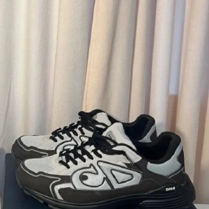 Grå Dior B30 sneakers i mesh - Snygga Dior B30 sneakers i grått och brunt med stora CD-loggor på sidorna. Skorna har en modern chunky sula, svart snörning och är tillverkade i mesh och syntetmaterial för en sportig vibe. Perfekta för dig som gillar exklusiva och trendiga sneakers.