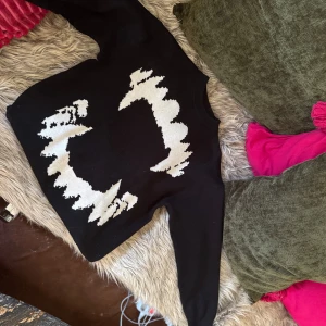 Svart stickad tröja med vit grafisk design - Cool svart stickad tröja med lång ärm och stor vit grafisk design framtill. Tröjan har en klassisk passform och är perfekt för dig som gillar unika prints och streetstyle. Passar lika bra till jeans som till kjol.