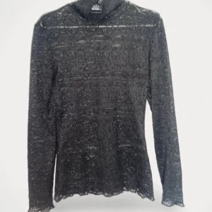 Svart spetsig långärmad topp - Svart långärmad topp från Soaked in Luxury med genombruten spets och snyggt mönster. Tunn och lätt, perfekt att styla lager på lager. Figurnära passform och fina detaljer vid ärmslut och hals.