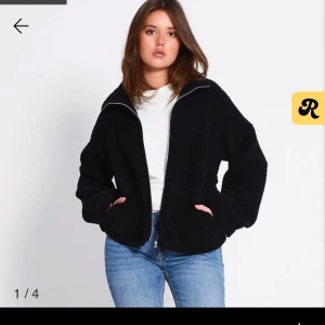 Svart teddyjacka med dragkedja - Mysig svart teddyjacka med hög krage och hel dragkedja framtill. Jackan har två stora fickor och en avslappnad passform som är perfekt för kyliga dagar. Materialet är fluffigt och ger en cool, casual vibe.