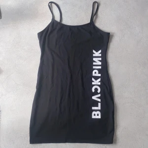 Svart kortklänning BLACKPINK  - Svart kortklänning från H&M Divided x BLACKPINK med smala axelband och vit logga längs sidan. Tight passform och tillverkad i mjuk bomull, perfekt för dig som gillar enkel men snygg stil.