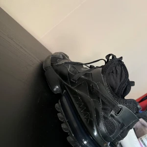Svarta Nike Air Max sneakers - Snygga helsvarta Nike Air Max sneakers med chunky sula och tydlig Air Max-detalj på sidan. Skorna har en mix av skinn och mesh, snörning och coola paneler som ger en sportig vibe. Perfekta för dig som gillar streetstyle och vill ha något som sticker ut.