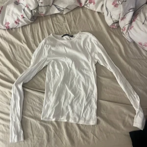 Vit långärmad tröja från 157 - En basic vit långärmad tröja från 157 i storlek XS. Tröjan har rund halsringning och är gjord i mjuk bomull, perfekt att styla med jeans eller kjol. Enkel och stilren design som funkar året runt.