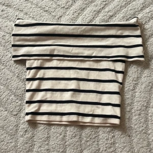 Randig offshoulder topp i bomull - Snygg offshoulder topp med svarta ränder på beige botten. Croppad modell som sitter tight och har en klassisk båtringning. 